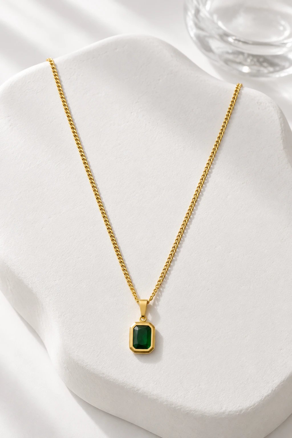 Collar de oro con colgante de piedra verde esmeralda sobre una piedra blanca